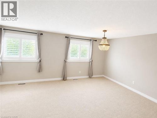 Bright room featuring a beaded chandelier, two windows with white plantation shutters, and light-colored carpet flooring - Upper-313 Featherstone Crescent, Kitchener, ON - Indoor