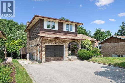 Brick and horizontal siding exterior featuring an attached garage with a brown door, an arched front entry, a paved driveway, and mature landscaping - 8 Perin Place, Kitchener, ON - Outdoor