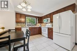 Kitchen featuring wood cabinetry, white appliances, tile flooring, and a decorative backsplash - 