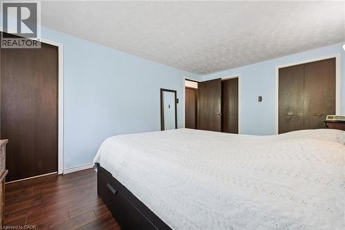 Spacious room featuring wood-finish flooring, two large closets with dark wood doors, light blue painted walls, and a textured white ceiling - 8 Perin Place, Kitchener, ON - Indoor Photo Showing Bedroom