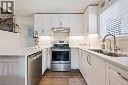 U-shaped kitchen featuring white shaker cabinetry, stainless steel appliances, a double basin sink with a gooseneck faucet, light-toned countertops, and wood-finish flooring - 