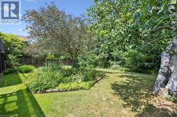 Spacious backyard featuring a manicured lawn, established garden beds with various plantings, and mature trees providing natural privacy - 