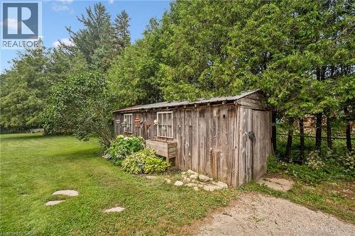 Rustic wooden shed with multiple windows, set against a backdrop of mature evergreen trees - 7988 Wellington Road 12, Arthur, ON - Outdoor