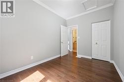 Room featuring wood-finish flooring, light grey walls, white baseboards, and crown molding - 