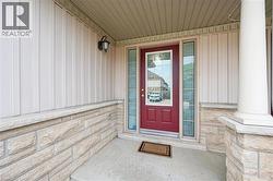 Welcoming entryway featuring a red door with decorative glass inserts, sidelight windows, a stone facade base, vertical panel siding, and a fluted column - 