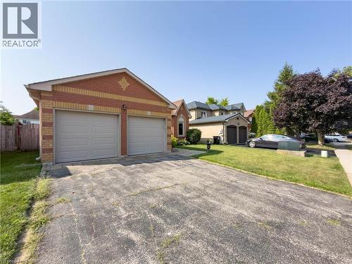 Brick exterior featuring a two-car garage with individual doors, a paved driveway, and a front yard with mature landscaping - 60 Attwood Drive, Cambridge, ON - Outdoor