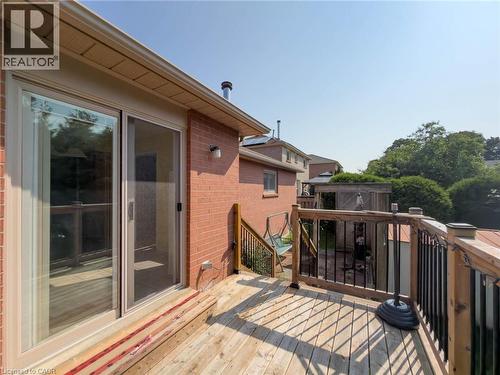 Expansive outdoor wooden deck featuring a wood railing with black metal spindles, a sliding glass door with screen, and a brick exterior wall - 60 Attwood Drive, Cambridge, ON - Outdoor With Exterior