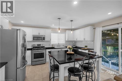Modern kitchen featuring white cabinetry, stainless steel appliances, a black countertop island, and tile flooring - 65 Thistlemoor Drive, Caledonia, ON - Indoor Photo Showing Kitchen With Upgraded Kitchen
