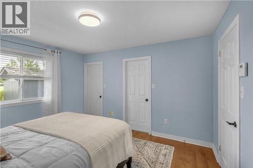 Bedroom featuring a window with blinds, wood-finish flooring, two paneled doors, and a ceiling-mounted light fixture - 65 Thistlemoor Drive, Caledonia, ON - Indoor Photo Showing Bedroom