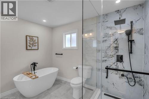 Modern bathroom featuring a freestanding soaking tub with a matte black floor-mounted faucet, a walk-in shower with a glass enclosure and marble-look tile surround, a built-in shower niche, and a rain - 65 Thistlemoor Drive, Caledonia, ON - Indoor Photo Showing Bathroom