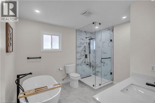 Bathroom featuring a frameless glass shower enclosure with marble-look wall tiling, a freestanding soaking tub with floor-mounted black fixtures, and a vanity with a white countertop and integrated si - 65 Thistlemoor Drive, Caledonia, ON - Indoor Photo Showing Bathroom