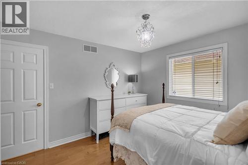 Room featuring light gray walls, wood-finish flooring, a white six-panel door with brass hardware, and a window with horizontal blinds - 65 Thistlemoor Drive, Caledonia, ON - Indoor Photo Showing Bedroom