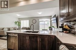 Kitchen island featuring a double-basin sink with a gooseneck faucet, light-toned countertop, and dark wood-finish cabinetry - 