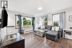 Living area featuring wood-finish flooring, white walls, and multiple windows with natural wood trim - 