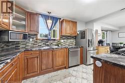 Kitchen featuring rich wood cabinetry, patterned stone countertops, a mosaic tile backsplash, stainless steel appliances, and tile flooring - 