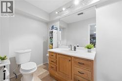 Bathroom featuring a wood-finish vanity with a white countertop and integrated sink, a toilet, and tiled flooring - 