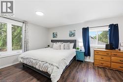 Bedroom featuring dark wood-finish flooring, light grey painted walls, and a large window with white trim - 