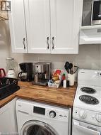 Compact kitchen area featuring white shaker-style cabinetry with dark-finish hardware, wood-finish countertops, and a white electric range - 