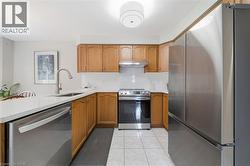 Kitchen featuring wood cabinetry, white countertops, stainless steel appliances, and tile flooring - 