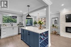 Kitchen featuring a large central island with integrated wine storage, white cabinetry, integrated stainless steel appliances, and engineered hardwood flooring - 