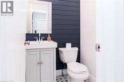 Powder room featuring a shiplap accent wall, white vanity with integrated sink, chrome faucet, and patterned floor tile - 