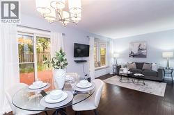 Open-concept dining and living area featuring dark wood-finish flooring, a contemporary chandelier, and a sliding glass door leading to an outdoor deck - 