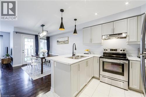 Open-concept kitchen featuring light-toned cabinetry, stainless steel appliances, a center island with a double sink, and white tile flooring - 1000 Asleton Boulevard Unit# 58, Milton, ON - Indoor Photo Showing Kitchen With Double Sink With Upgraded Kitchen