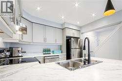 Kitchen featuring a double basin stainless steel sink with a matte black faucet, white countertops with veining, light gray cabinetry with brushed nickel hardware, and stainless steel appliances - 