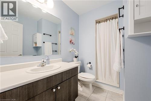 Bathroom featuring a wood-finish vanity with an integrated sink and light-toned countertop, a large wall-mounted mirror, a shower with a white curtain, and tile flooring - 1000 Asleton Boulevard Unit# 58, Milton, ON - Indoor Photo Showing Bathroom