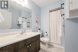 Bathroom featuring a wood-finish vanity with an integrated sink and light-toned countertop, a large wall-mounted mirror, a shower with a white curtain, and tile flooring - 