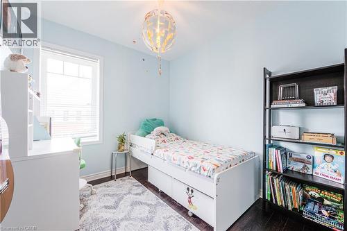 Bright room featuring a window with white blinds, dark wood-finish flooring, and a decorative overhead light fixture - 1000 Asleton Boulevard Unit# 58, Milton, ON - Indoor Photo Showing Bedroom