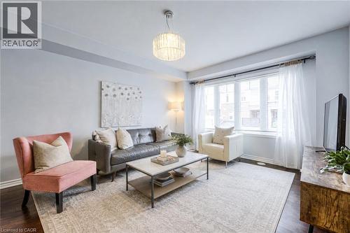 Spacious living area featuring dark wood-finish flooring, a large window with sheer drapes, a decorative ceiling light fixture, and crown molding - 1000 Asleton Boulevard Unit# 58, Milton, ON - Indoor Photo Showing Living Room