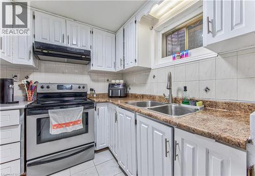 White cabinetry with brushed nickel hardware, stainless steel electric range, dual basin stainless steel sink, speckled countertops, and tiled backsplash - 2560 Palisander Avenue, Mississauga, ON - Indoor Photo Showing Kitchen With Double Sink
