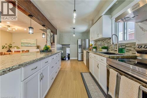 Kitchen featuring wood-finish flooring, white cabinetry, a large center island with a granite countertop, stainless steel appliances, and a mosaic tile backsplash - 2560 Palisander Avenue, Mississauga, ON - Indoor Photo Showing Kitchen With Upgraded Kitchen