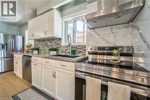 Kitchen featuring white cabinetry with brushed nickel hardware, granite countertops, a mosaic tile backsplash, stainless steel appliances, and a marble-look slab backsplash behind the range - 2560 Palisander Avenue, Mississauga, ON - Indoor Photo Showing Kitchen With Upgraded Kitchen