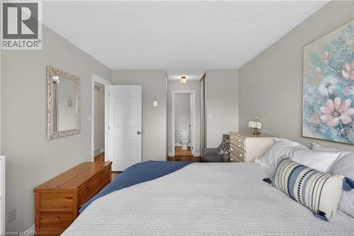 Bedroom featuring light gray wall paint, wood-finish flooring, white paneled doors, and a partial view of a bathroom with a white toilet - 56 Brookstream Court, Hamilton, ON - Indoor Photo Showing Bedroom
