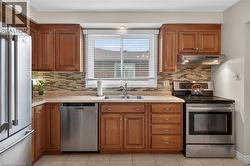 Kitchen featuring warm wood cabinetry, stainless steel appliances, a mosaic tile backsplash, a double basin sink, and neutral tile flooring - 