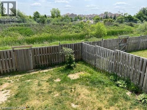 Fenced backyard featuring a grassy area, a wooden privacy fence with two gates, and a natural green expanse beyond the property line - 300 Countrystone Crescent, Kitchener, ON - Outdoor