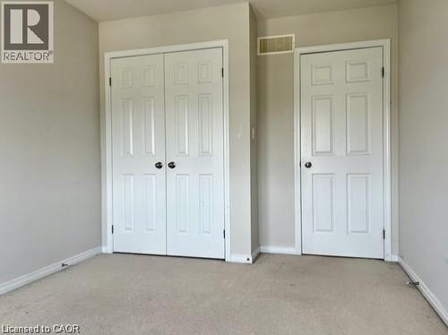 Neutral-toned room featuring a double bifold closet door, a single paneled door, and light beige carpet flooring - 300 Countrystone Crescent, Kitchener, ON - Indoor