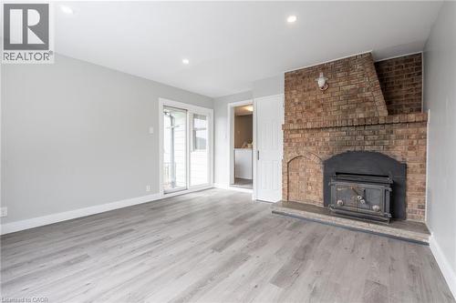 Expansive room featuring a brick fireplace with a wood-burning stove, light wood-finish flooring, and recessed ceiling lighting - 156 Adeline Avenue, Hamilton, ON 