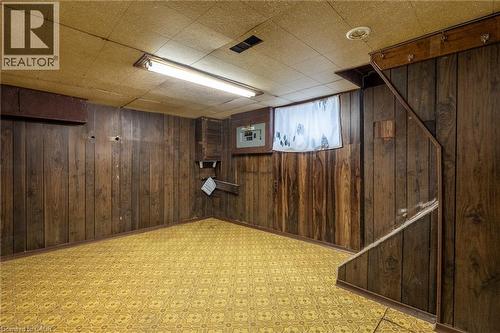 Lower-level room featuring wood-finish wall paneling, patterned flooring, a drop ceiling, and exposed overhead lighting - 156 Adeline Avenue, Hamilton, ON 