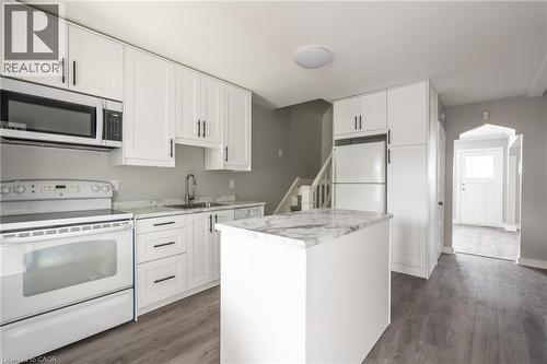 Modern kitchen featuring white cabinetry with dark hardware, a center island with a stone-finish countertop, wood-finish flooring, and white appliances - 156 Adeline Avenue, Hamilton, ON 