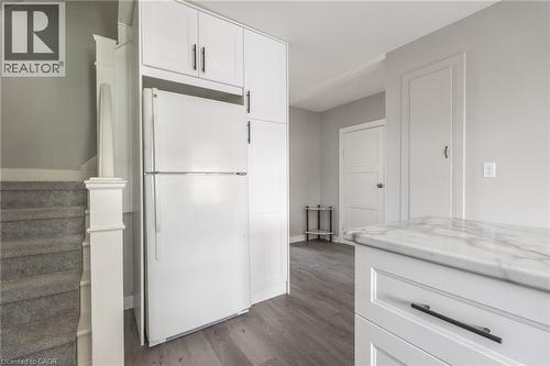 Full-height white cabinetry with black hardware, integrated refrigeration, wood-finish flooring, and a marble-finish countertop - 156 Adeline Avenue, Hamilton, ON 
