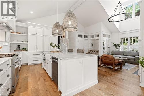Open-concept kitchen with vaulted ceilings, natural wood-finish flooring, white cabinetry, a central island with a white countertop, and stainless steel appliances - 330 Camelot Court, Burlington, ON - Indoor Photo Showing Kitchen