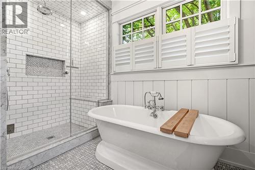 Freestanding soaking tub with chrome fixtures, glass-enclosed shower with subway tile, built-in shower bench, recessed shower niche, and white louvered window shutters - 330 Camelot Court, Burlington, ON - Indoor Photo Showing Bathroom