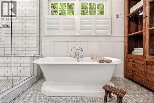 Freestanding soaking tub with a wall-mounted faucet, complemented by a glass-enclosed shower with subway tile surround and a herringbone pattern floor - 330 Camelot Court, Burlington, ON - Indoor Photo Showing Bathroom