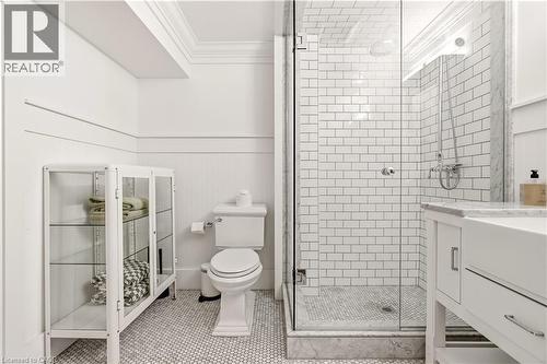 Subway tile shower with glass enclosure, penny tile flooring, marble shower curb, pedestal toilet, and white beadboard wainscoting - 330 Camelot Court, Burlington, ON - Indoor Photo Showing Bathroom