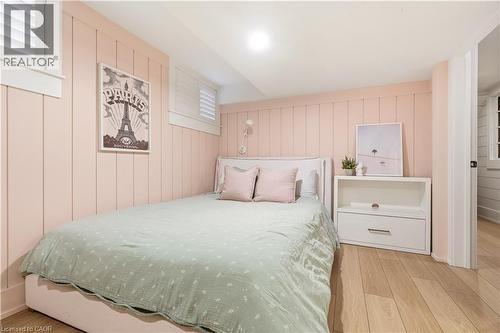 Room featuring light wood-finish flooring, vertical paneling on walls, and white plantation shutters on two windows - 330 Camelot Court, Burlington, ON - Indoor Photo Showing Bedroom