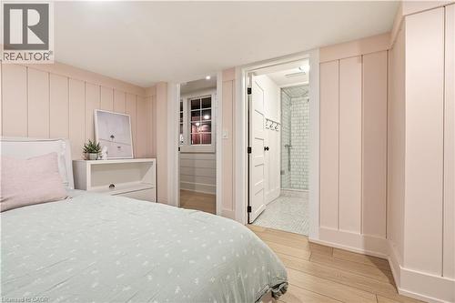 Bedroom featuring light wood-finish flooring, vertical paneling with baseboards, a built-in white nightstand, and an entryway to a full bathroom with a tiled shower - 330 Camelot Court, Burlington, ON - Indoor Photo Showing Bedroom