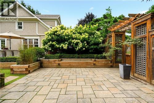 Expansive stone paver patio featuring a wooden pergola, raised garden beds, and mature landscaping - 330 Camelot Court, Burlington, ON - Outdoor